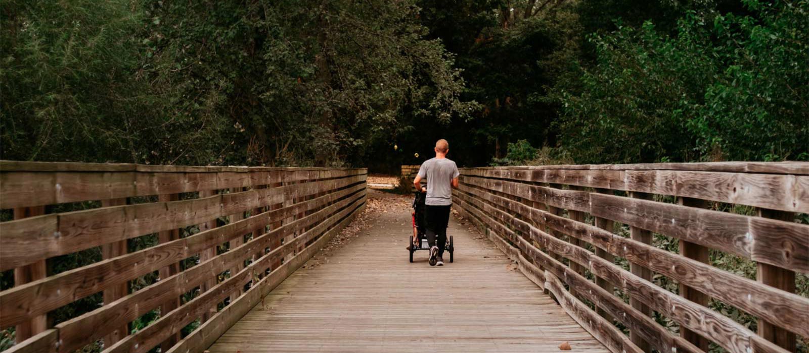 a person walking and pushing a stroller on a bridge on the trail